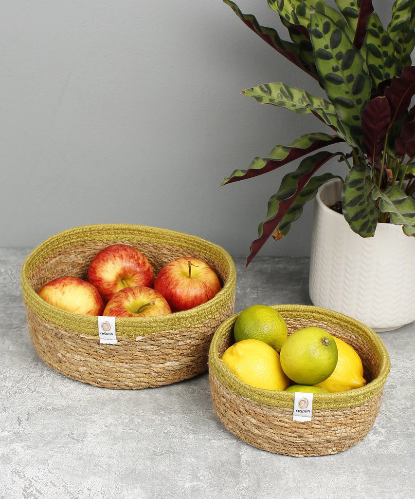 Respiin set of 2 natural shallow seagrass jute baskets with green rim. Showing each basket on a kitchen counter filled with fruit