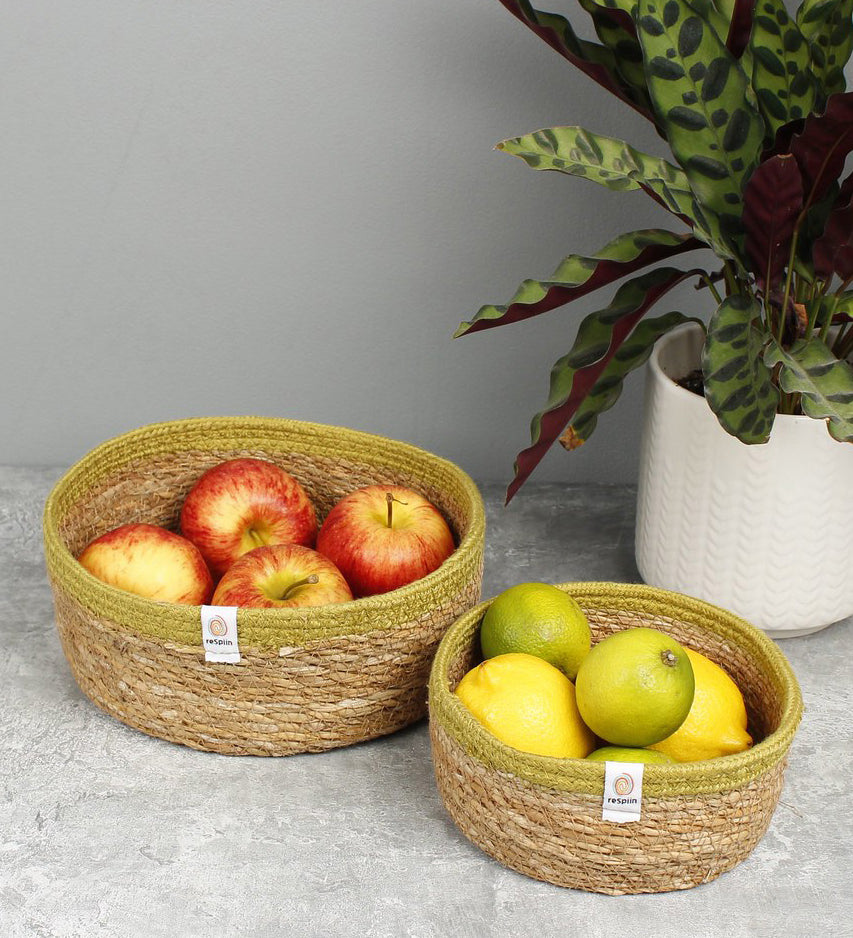 Respiin set of 2 natural shallow seagrass jute baskets with green rim. Showing each basket on a kitchen counter filled with fruit