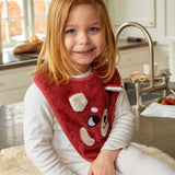 A child sat in a kitchen, wearing the Roommate Organic Cotton Baby Bib - Red Panda