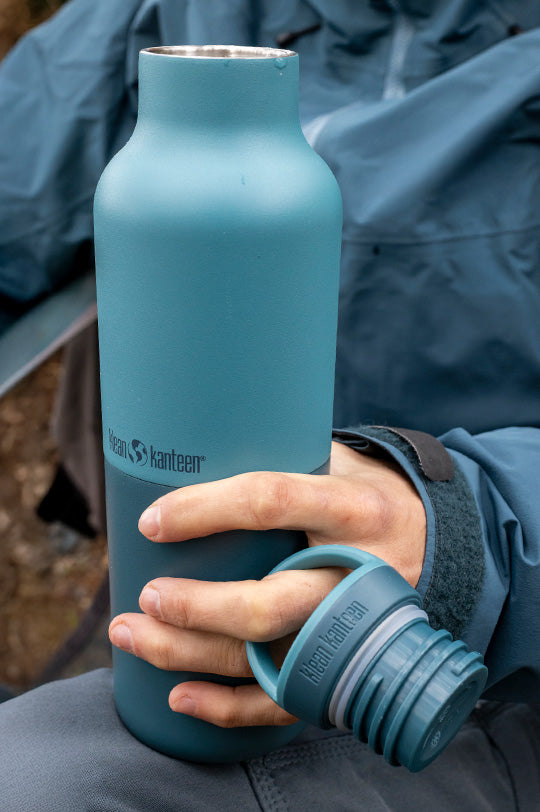 Hand holding a reusable Klean Kanteen stainless steel bottle in two tones of turquoise, leakproof and insulated, to represent Klean Kanteen Rise Collection for sale at Babipur, official UK stockist.