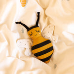 The Roommate Organic Cotton Bee Rattle, laying on a white/cream Roommate bed cover