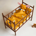 A Roommate teddy looking fast asleep in a baby bed, underneath the Roommate Doll Bedding Set - Tiger