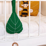 The Roommate Leaf Lullaby Music Mobile is attached to a white crib, and in the background is  Roommate yellow leaf cushion and a Roommate Bee Rag Doll