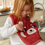 A child sat in a kitchen looking down at the Roommate Organic Cotton Baby Bib - Red Panda