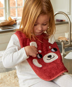 A child sat in a kitchen looking down at the Roommate Organic Cotton Baby Bib - Red Panda