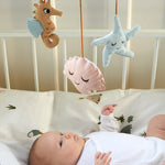 A baby laying in a crib, looking up at the Roommate Sealife Hanging Mobile