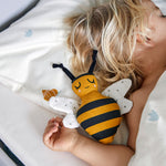 A child is sleeping with the Roommate Organic Cotton Bee Rattle next to them