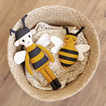 The Roommate Organic Cotton Bee Rattle in a basket with another Roommate bee toy, on a wooden floor background