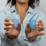 A person holding a large and small blue Silicone, BPA free and latex free Ruby Cup in between their fingers