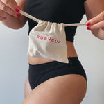 The drawstring storage bag which comes with the Ruby Cup menstrual cup, being held by a person who is pulling the drawstrings of the bag outwards