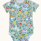 The farmyard all over print vest from the two pack of Frugi short sleeve baby vests. The print features farm animals, tractors, leaves and plants on a light blue background.