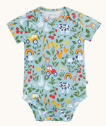 The farmyard all over print vest from the two pack of Frugi short sleeve baby vests. The print features farm animals, tractors, leaves and plants on a light blue background.