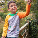 A child smiling, sitting on a gate wearinga Frugi Compass Organic Cotton Hooded Top. 