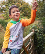 A child smiling, sitting on a gate wearinga Frugi Compass Organic Cotton Hooded Top. 