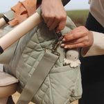 An adult clipping on the Avery Row Nappy Changing Bag - Sage, onto the side of a pram handle