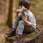 A child is sat on a large, cut tree stump, looking off into the distance, whilst holding the Senger Baby Mouse