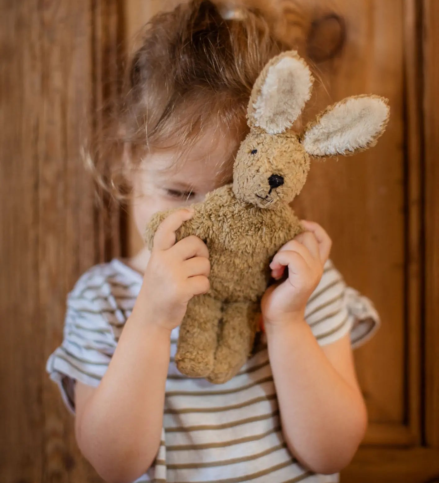 Senger baby rabbit in beige, made with organic cotton and stuffed with wool, held by child.