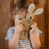 Senger baby rabbit in beige, made with organic cotton and stuffed with wool, held by child.