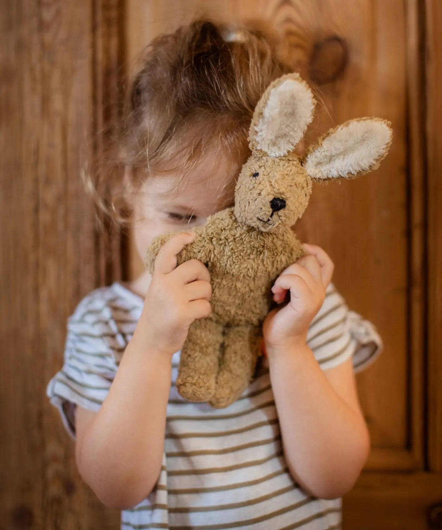 Senger baby rabbit in beige, made with organic cotton and stuffed with wool, held by child.