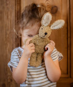 Senger baby rabbit in beige, made with organic cotton and stuffed with wool, held by child.
