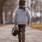 A child walking down a deserted road, whilst carrying the Senger Baby Mouse in a green jug with their left hand. The image shows the child from the back and the Senger Baby Mouse in the jug being held down by the child's left knee