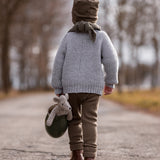 A child walking down a deserted road, whilst carrying the Senger Baby Mouse in a green jug with their left hand. The image shows the child from the back and the Senger Baby Mouse in the jug being held down by the child's left knee