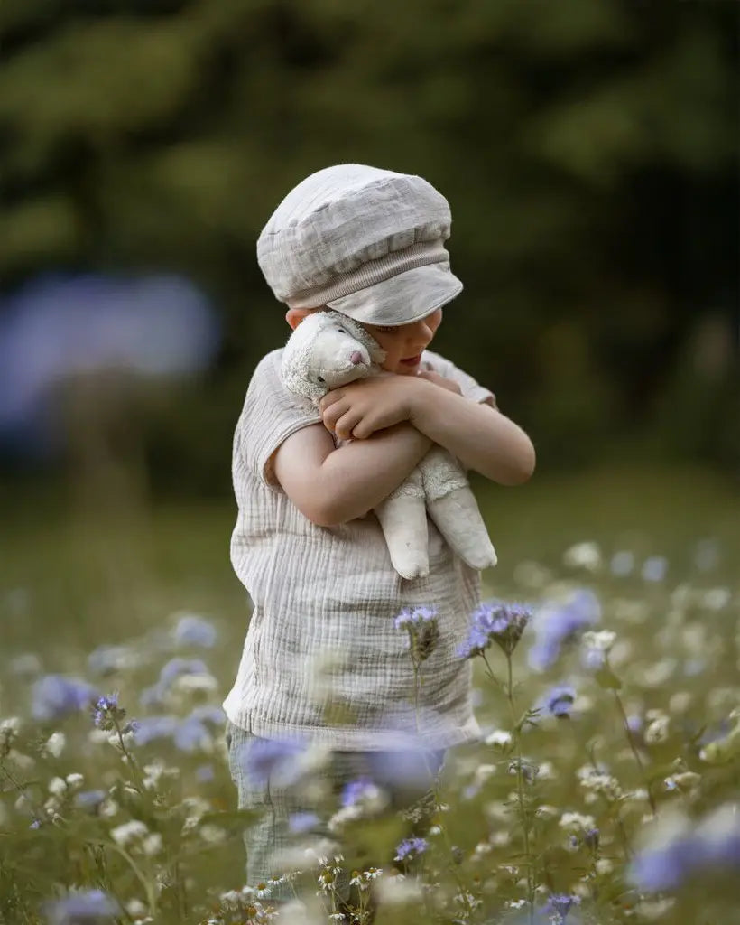 Senger Floppy White Sheep, a small cuddly toy made from organic cotton filled with wool, in child's arm in a field of flowers.