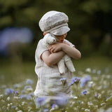 Senger Floppy White Sheep, a small cuddly toy made from organic cotton filled with wool, in child's arm in a field of flowers.