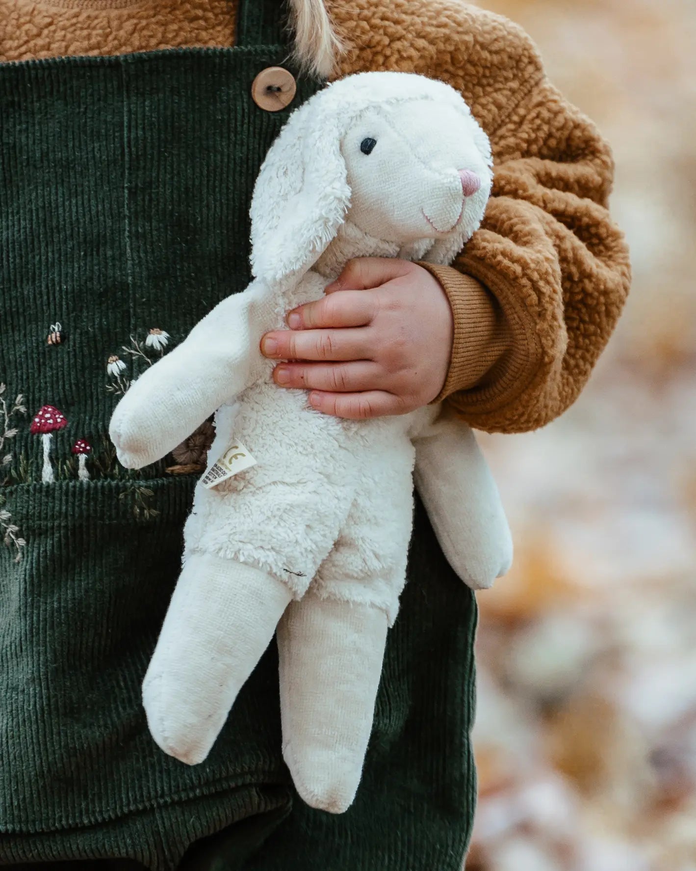 Senger White Sheep, a small floppy soft toy made from organic cotton and wool, in child's arm.