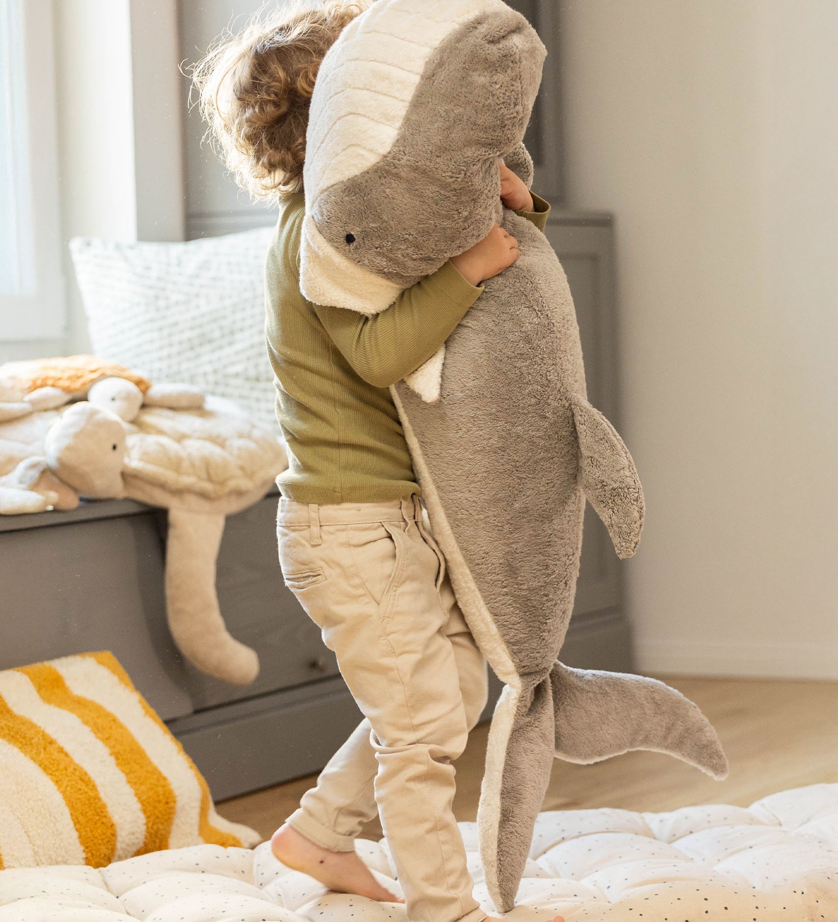 A child holding the Senger giant grey soft and cuddly whale toy showing the size of the toy. This soft toy is available at Babipur.