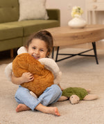 A child is smiling happily and is holding a larger Senger Cuddly Turtle with a brown shell. The Small Cuddly Turtle is next to the child
