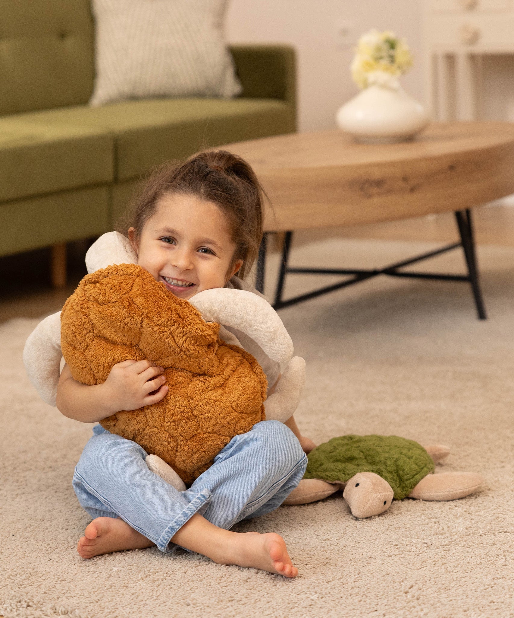A child is smiling happily and is holding a larger Senger Cuddly Turtle with a brown shell. The Small Cuddly Turtle is next to the child