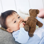 A child holding the arm of the Senger Baby Brown Bear next to their mouth