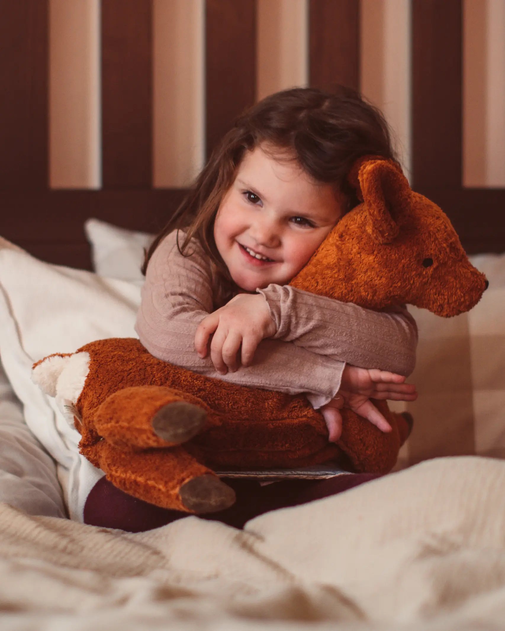 Senger Naturwelt Large Cuddly Deer Organic Soft Toy, made from wool and organic cotton, held by child on bed.