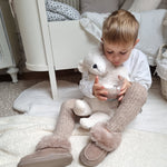 A child sat on a fluffy white rug in their room, holding the Senger Large Cuddly Polarbear in their arms and a cup of hot chocolate