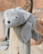 Senger Naturwelt Small Cuddly Grey Seal Organic Soft Toy, made from wool and organic cotton on a log at the beach.