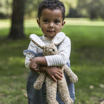 A child outside in a grassy field, holding the Senger Small Floppy Beige Rabbit in their arms
