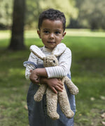 A child outside in a grassy field, holding the Senger Small Floppy Beige Rabbit in their arms