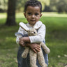 A child outside in a grassy field, holding the Senger Small Floppy Beige Rabbit in their arms