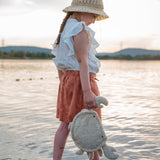 A small child standing in water and holding the cream coloured Senger Naturwelt small cuddly crab in a light beige colour by the claw