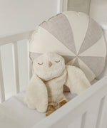 A GOTS organic cotton snowy owl soft toy by Senger available at Babipur sitting upright in a cot showing the cute, sleepy facial features.
