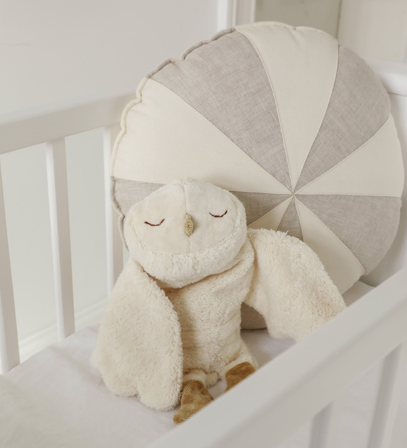A GOTS organic cotton snowy owl soft toy by Senger available at Babipur sitting upright in a cot showing the cute, sleepy facial features.