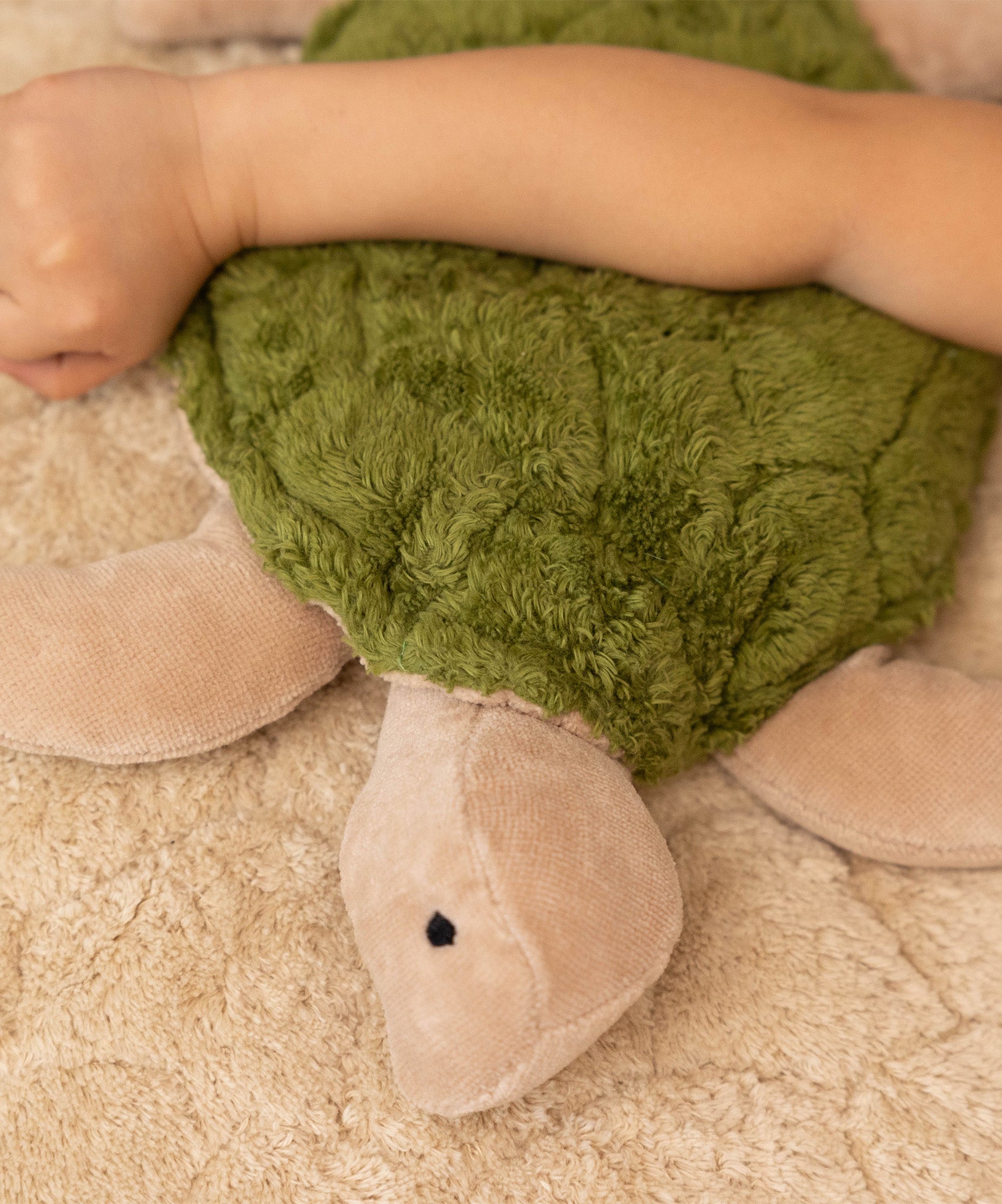 A closer look at the head and shell of the Senger Cuddly Turtle - Green. The head and flippers of the Turtle are a very light brown/beige colour and it has a small black eye. The shell is green and fluffy, and has lines to give the effect of a real turtle shell