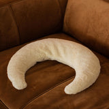 A Senger nursing and neck cushion on a brown chair. This white moon shaped cushion is available at Babipur. 