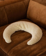 A Senger nursing and neck cushion on a brown chair. This white moon shaped cushion is available at Babipur. 