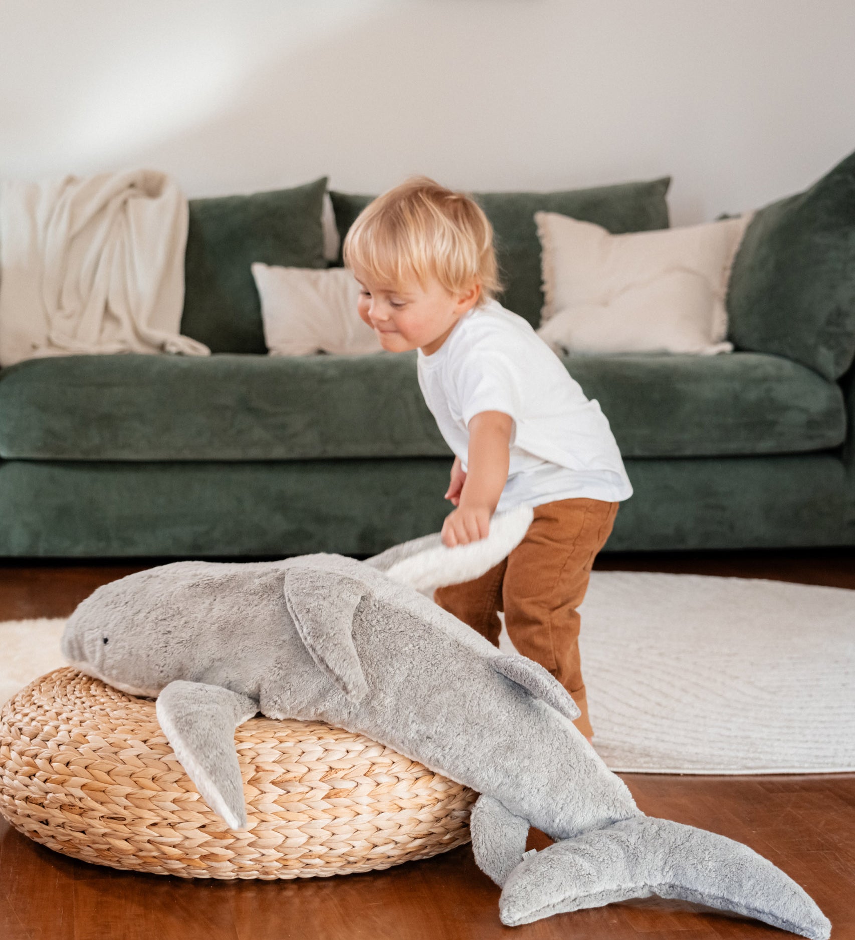 A small child playing and holding the fin of the grey Senger Naturwelt XL Cuddly Shark, organic GOTS cotton plush soft toy with removable spelt husk heat cushion.