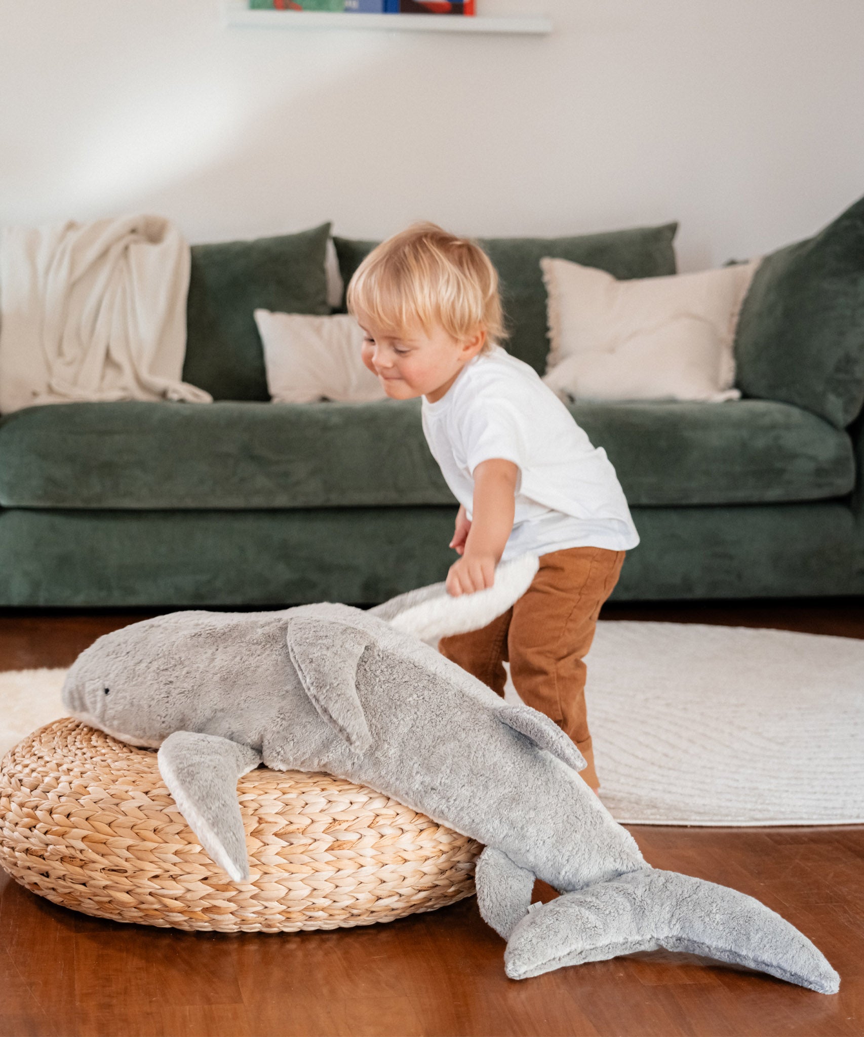 A small child playing and holding the fin of the grey Senger Naturwelt XL Cuddly Shark, organic GOTS cotton plush soft toy with removable spelt husk heat cushion.