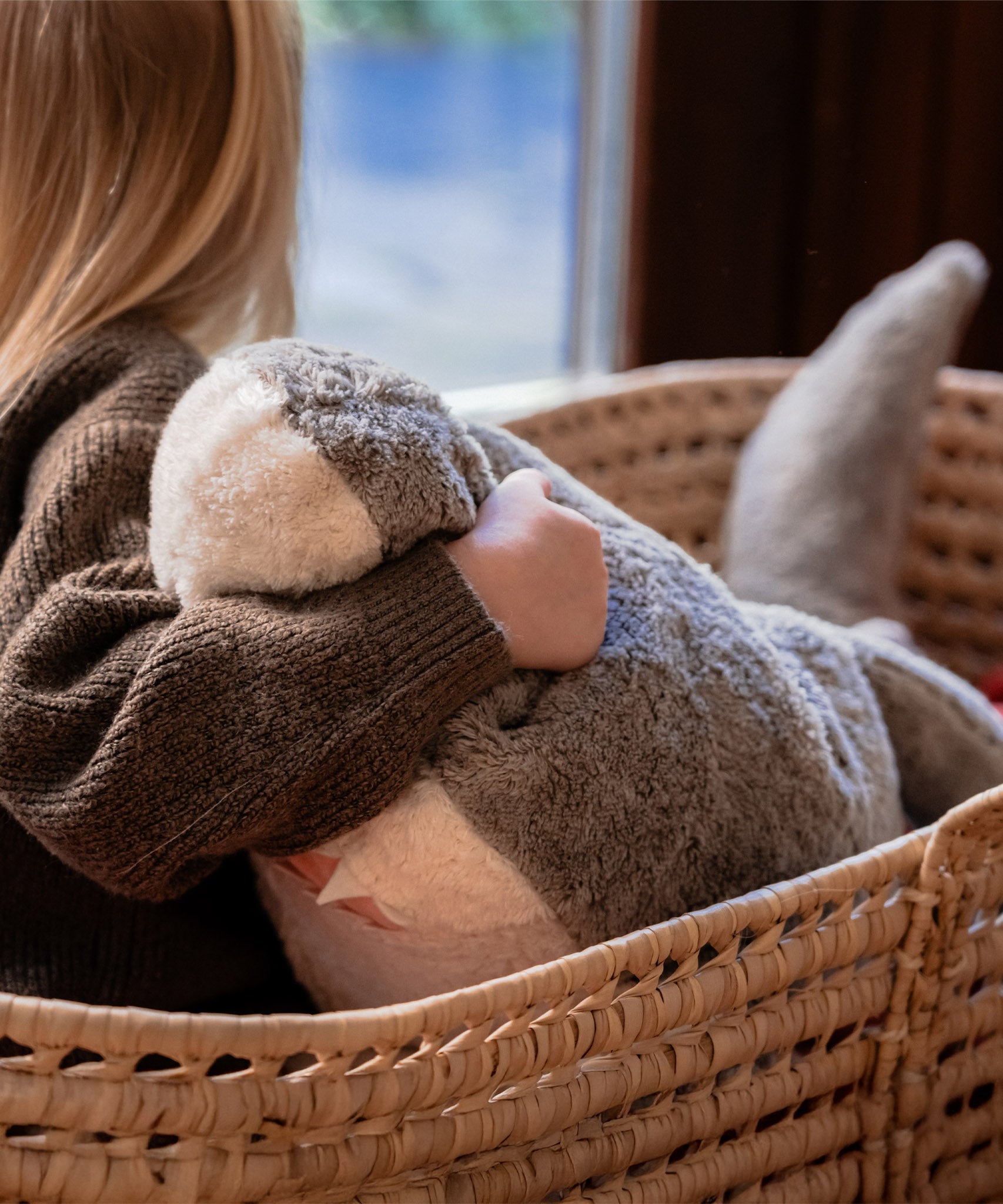 A close up of a child sitting in a basket and holding the Senger Naturwelt Large Cuddly Shark showing the teeth detail on the mouth
