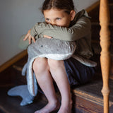 A child sitting on wooden stairs and resting their head and arms on the grey Senger Naturwelt Large Cuddly Shark, 