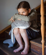 A child sitting on wooden stairs and resting their head and arms on the grey Senger Naturwelt Large Cuddly Shark, 